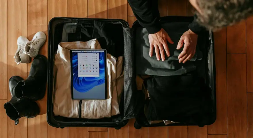 Osoba pakuje walizkę, w której widać ubrania, buty i tablet z ekranem Windows.