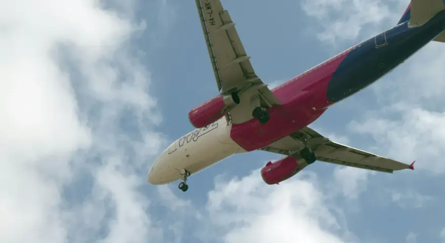 Samolot Wizzair w locie, widok od dołu, na tle błękitnego nieba z chmurami.