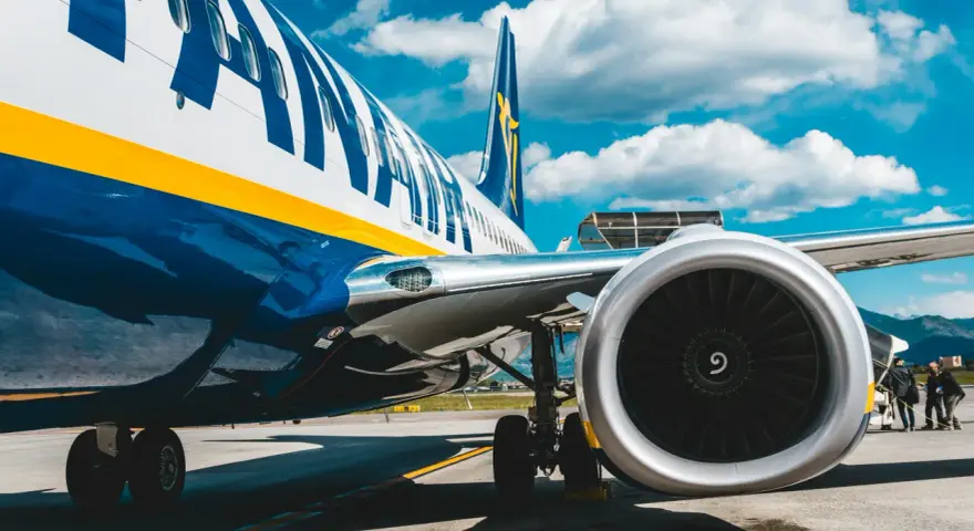 Fragment samolotu Ryanair z widocznym silnikiem i podwoziem na tle nieba.