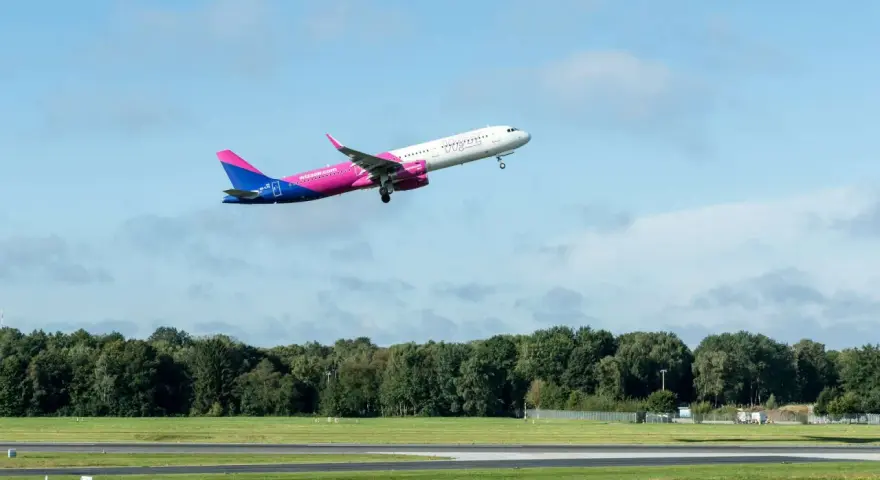 Samolot Wizz Air wznosi się na tle błękitnego nieba z chmurami.