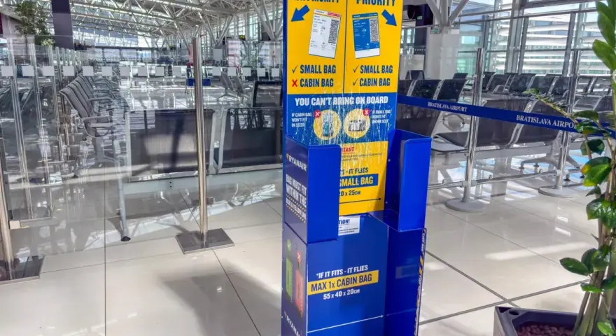 Niebieski stojak Ryanair z informacjami o bagażu w poczekalni lotniskowej.