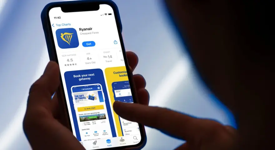 Dłoń trzyma smartfon z otwartą aplikacją Ryanair, widoczny ekran z logo i opcjami.