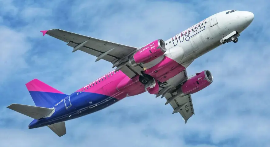 Samolot Wizz Air z różowymi silnikami i ogonem wznosi się na tle błękitnego nieba.