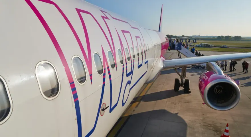 Samolot Wizz Air z pasażerami wsiadającymi po schodkach na lotnisku.