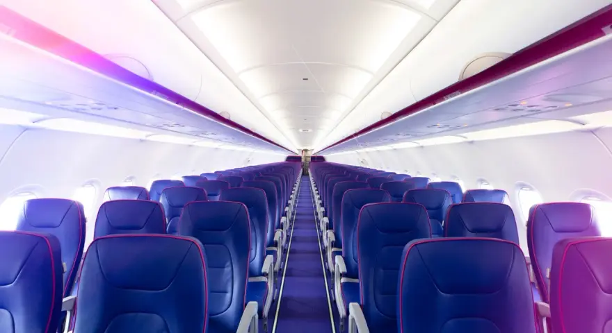 Wnętrze samolotu Wizz Air z rzędami niebieskich foteli i fioletowym oświetleniem.