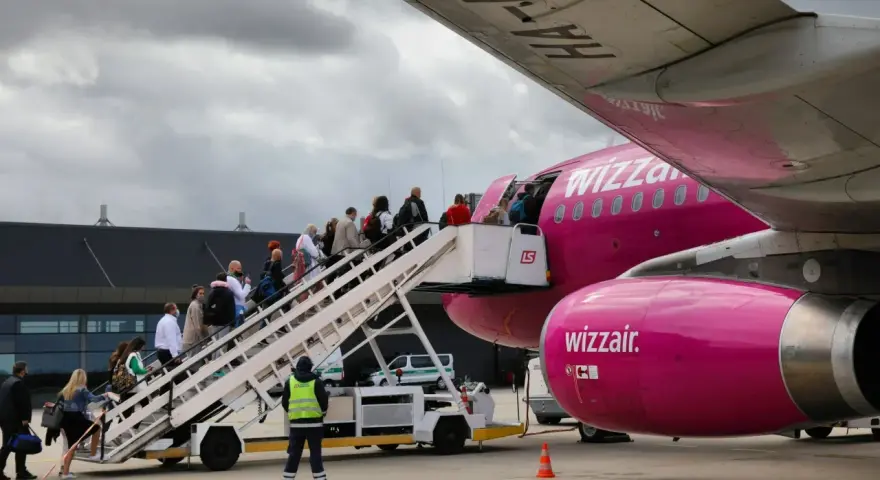 Pasażerowie wsiadają po schodkach do różowego samolotu Wizz Air.