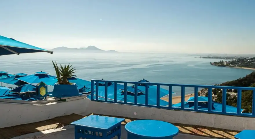 Widok na morze z niebieskimi parasolami i stolikami na tarasie.