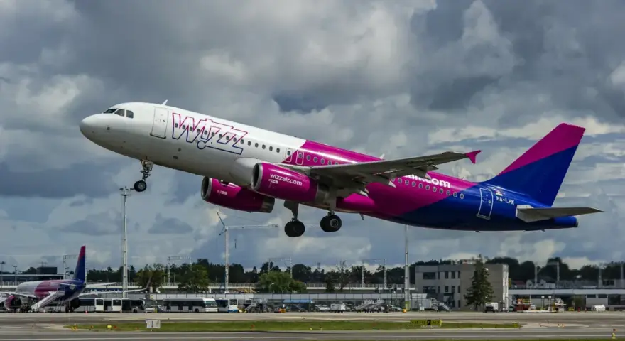 Samolot Wizz Air z różowymi silnikami startuje na tle chmur.