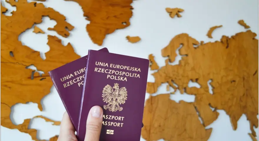 Dłoń trzyma dwa polskie paszporty na tle drewnianej mapy Europy.