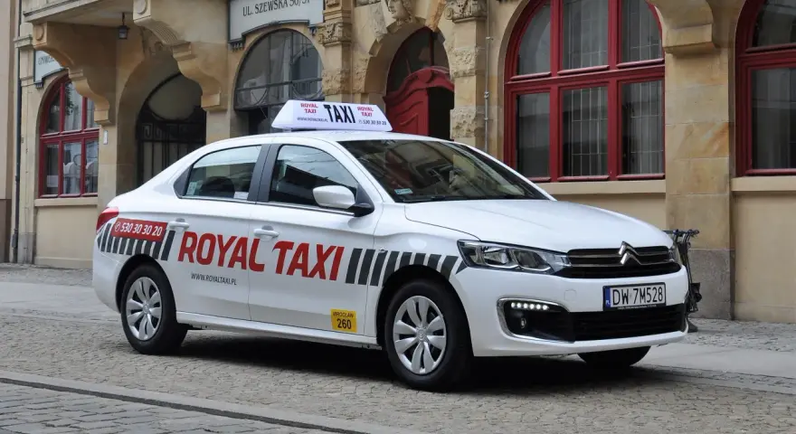 Biała taksówka Royal Taxi z numerem 260 na tle zabytkowej kamienicy we Wrocławiu.