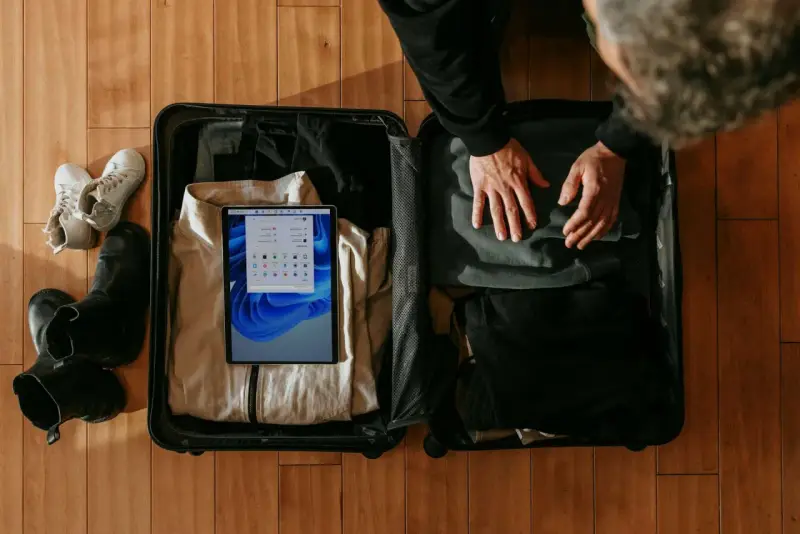 Osoba pakuje walizkę, w której widać ubrania, buty i tablet z ekranem Windows.